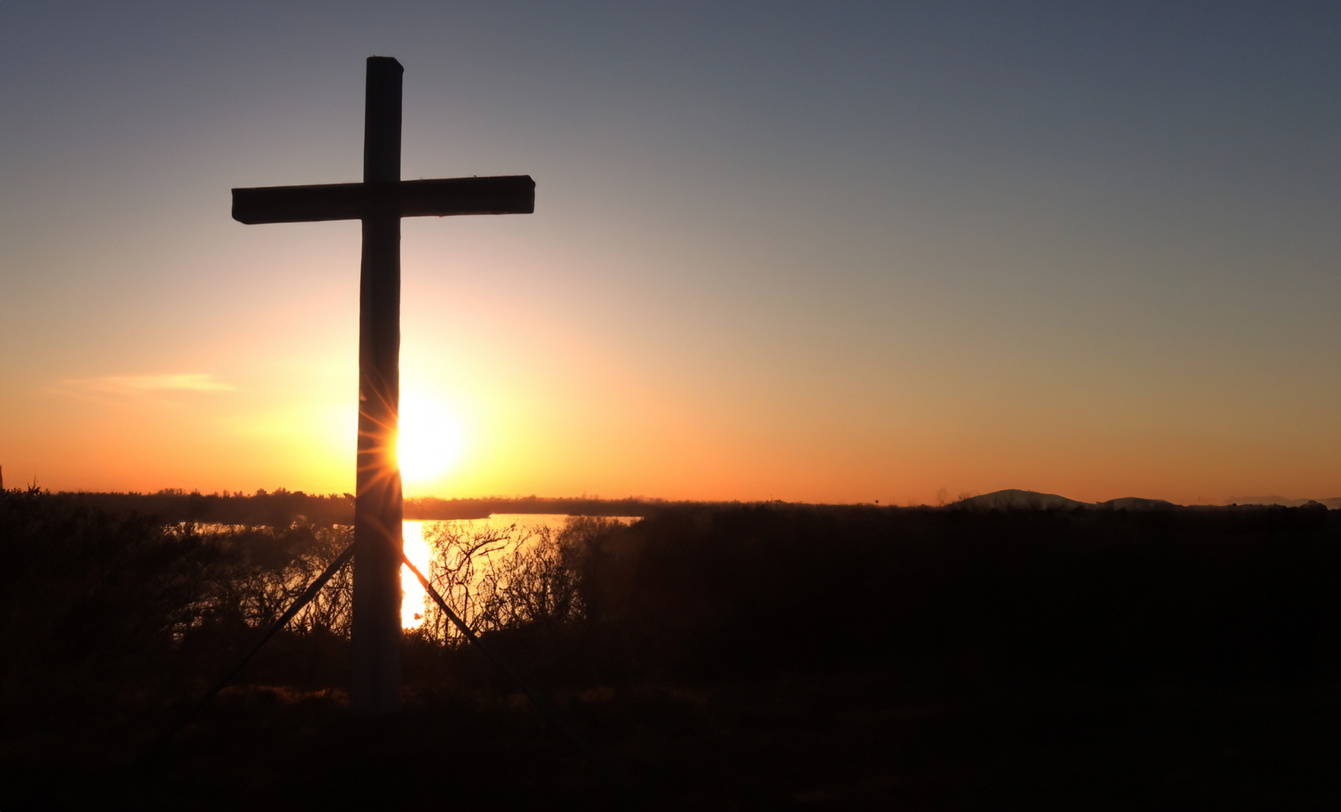 The cross standing on meadow sunset and flare background. Cross on a hill as the morning sun comes up for the day. The cross symbol for Jesus Christ. Easter background concept and The crosses sign.